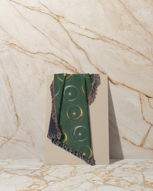 Forest green cotton throw blanket with woven silver moon phases and golden sun motifs, finished with multicolored fringe trim.